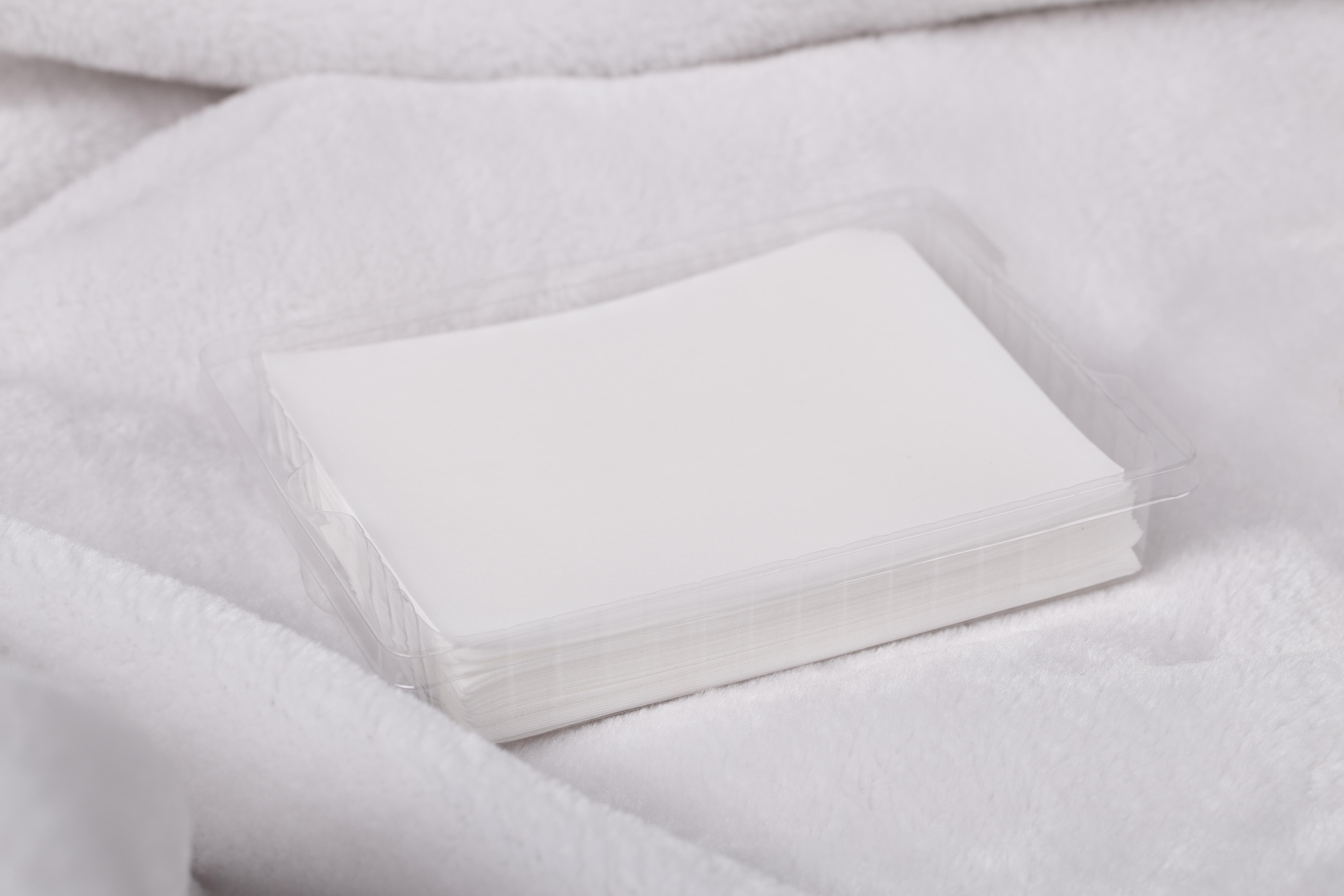 Close up of a bunch of dryer sheets, sitting on a white cloth . Dryer in the background.